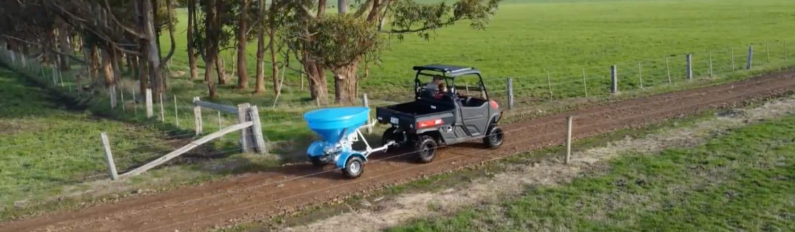 Aerial view of a farm vehicle towing a spreader down a farm track