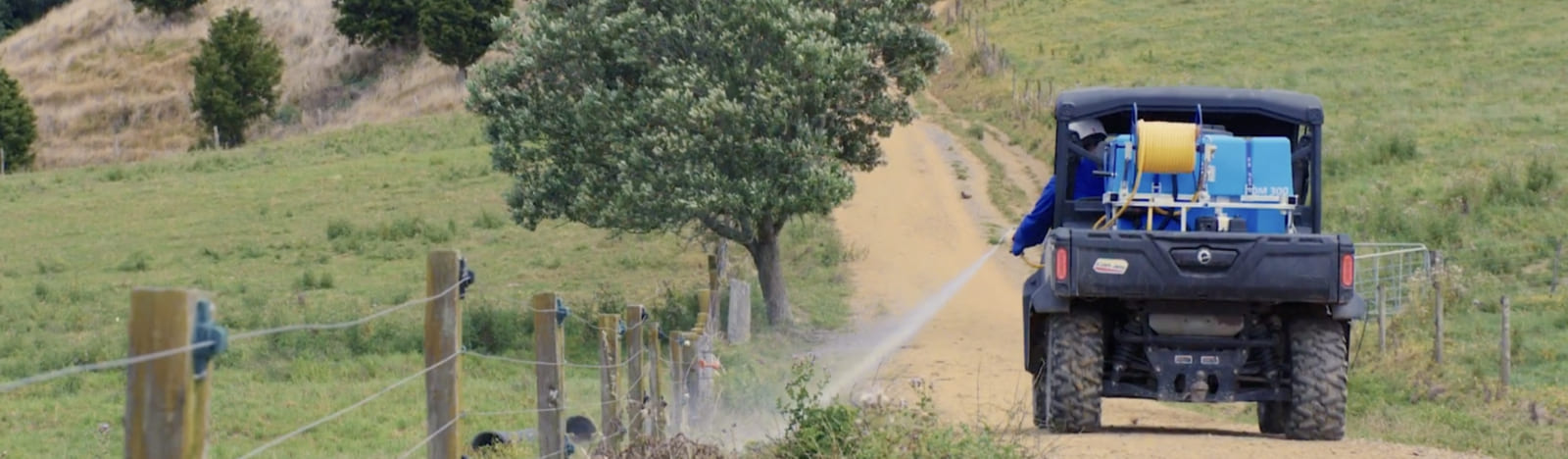 A person in safety gear spraying the fenceline using a deckmount sprayer on the back of their farm vehicle