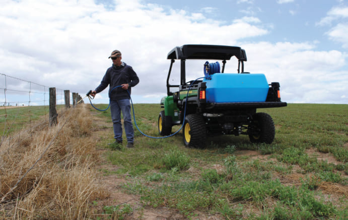 Man using an EZI-Spot Sprayer on the back of his farm vehicle to spray the fenceline