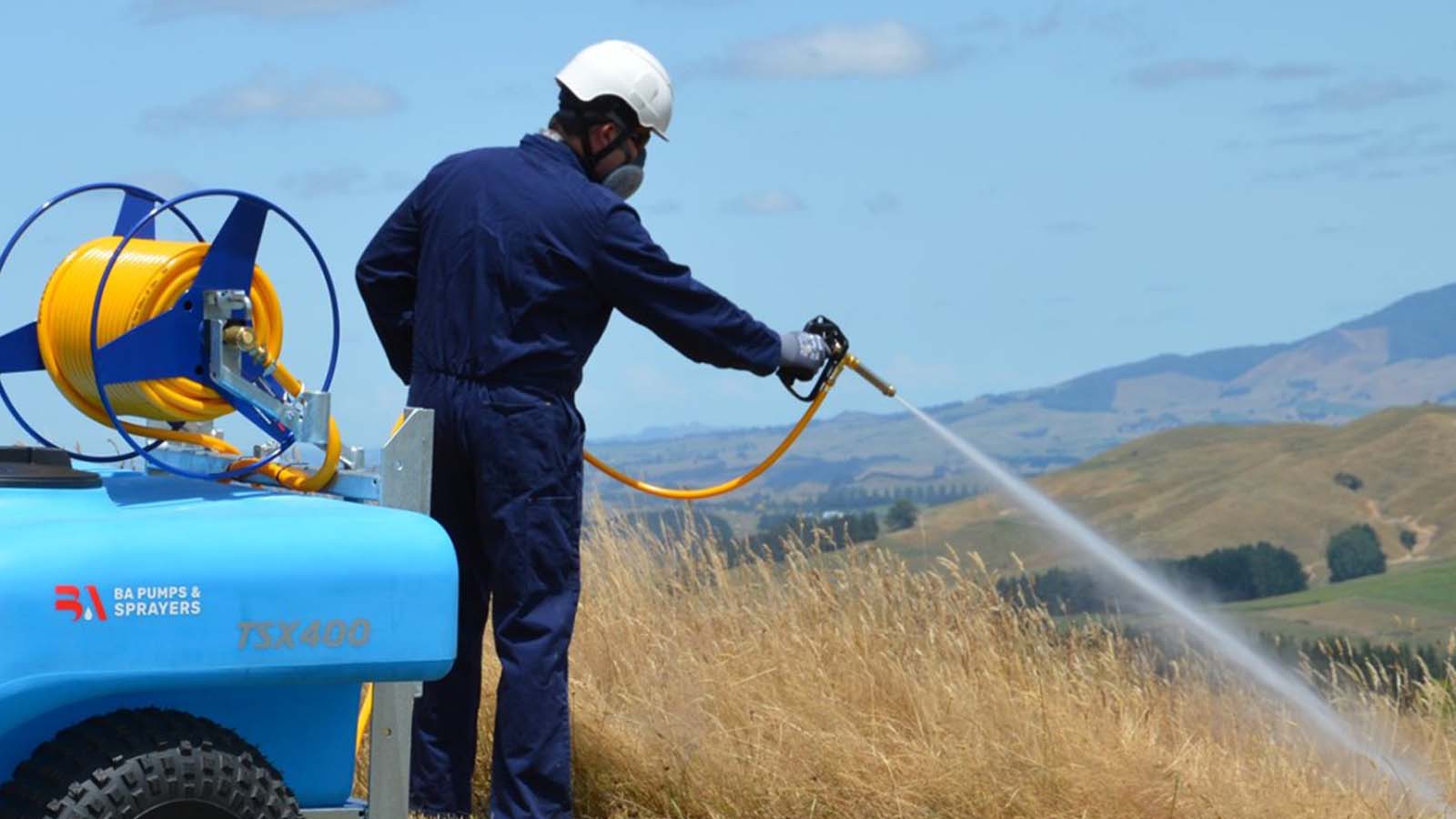 Person in PPE gear spraying weeds with a spray gun