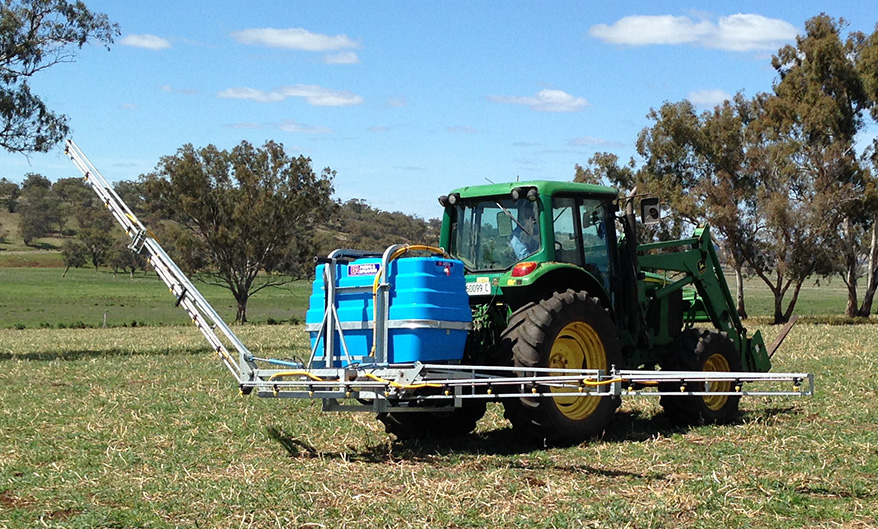 Spray boom spraying on the back of a tractor in a field.